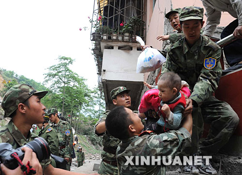 5月13日，在震后的北川縣城，武警戰(zhàn)士將一名和家人失散的幼童救出。 記者從四川省綿陽市抗震救災指揮部了解到，受災特別嚴重的北川縣老縣城80%、新縣城60%以上的建筑物因地震垮塌，縣城周邊發(fā)生大面積山體滑坡。
