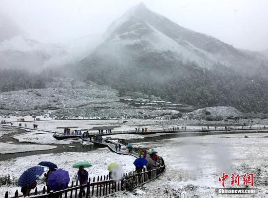 9月20日，受冷空氣影響，四川甘孜州稻城亞丁景區(qū)雪花飄舞，大霧彌漫，山峰披上白紗，銀裝素裹。正在景區(qū)內游玩的海內外游客紛紛用手機記錄雪景，并拍照留念。鐘欣 攝