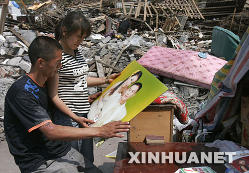 5月19日，雖然相框損壞了，夫妻倆還是仔細地把結婚照擦拭干凈。 四川省什邡市鎣華鎮(zhèn)仁和村三組的梁正彬一家很幸運，大地震發(fā)生時，包括老父母和年幼女兒在內(nèi)的全家5口人都跑出了轟然倒塌的房屋?！捌桨簿褪歉?！”他們默默收拾廢墟中的家，準備重建家園。